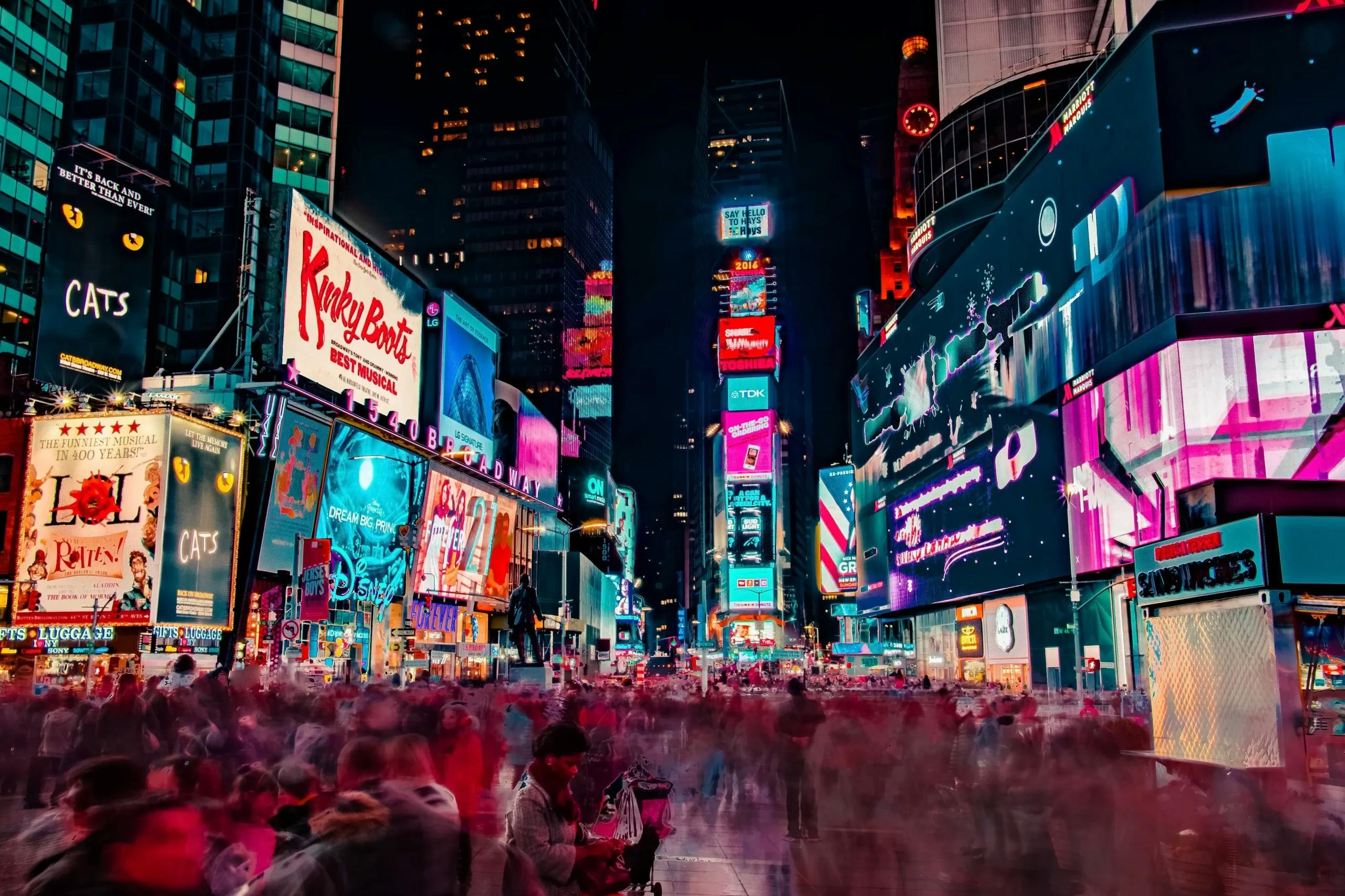 Vibrant night scene at Times Square with illuminated billboards for Broadway shows and a bustling crowd in motion